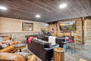 A cozy log cabin interior with leather sofas, a foosball table, and a large painting of a mountain landscape. - Cozy Lodge w/Theater|Firepit|Arcade|Hot Tub (Gatlinburg)
