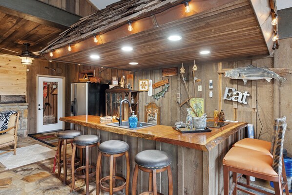 A rustic kitchen with a wooden bar, stools, and various kitchen appliances. - Cozy Lodge w/Theater|Firepit|Arcade|Hot Tub (Gatlinburg)