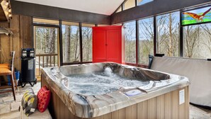 Una bañera de hidromasaje en una habitación con ventanas amplias, un armario rojo y vistas a árboles.