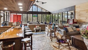 Amplia sala de estar con piso de piedra, muebles de madera y ventanas grandes que ofrecen vistas al exterior.