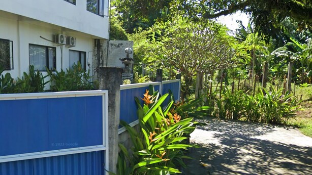 Un edificio con una valla azul, rodeado de exuberante vegetación y árboles.