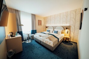 Une chambre d’hôtel équipée d’un lit, de tables de chevet, d’un bureau, d’une poubelle et d’une fenêtre avec des rideaux.