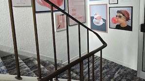 A staircase with a metal railing leading to a landing where various framed artworks are displayed on the wall. - guestified. LIYANA Hotel (Ratingen)