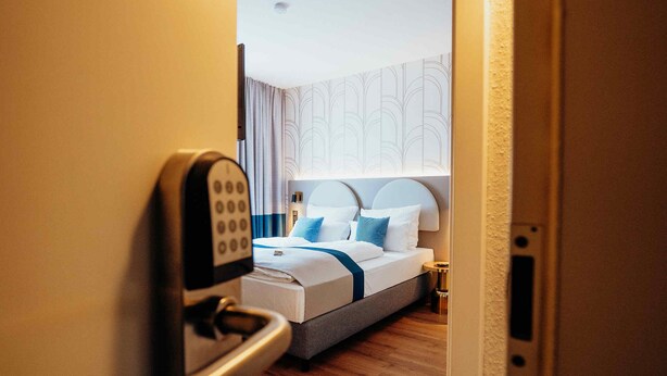 A hotel room with a bed, a bedside table, and a modern door lock. - guestified. LIYANA Hotel (Ratingen)