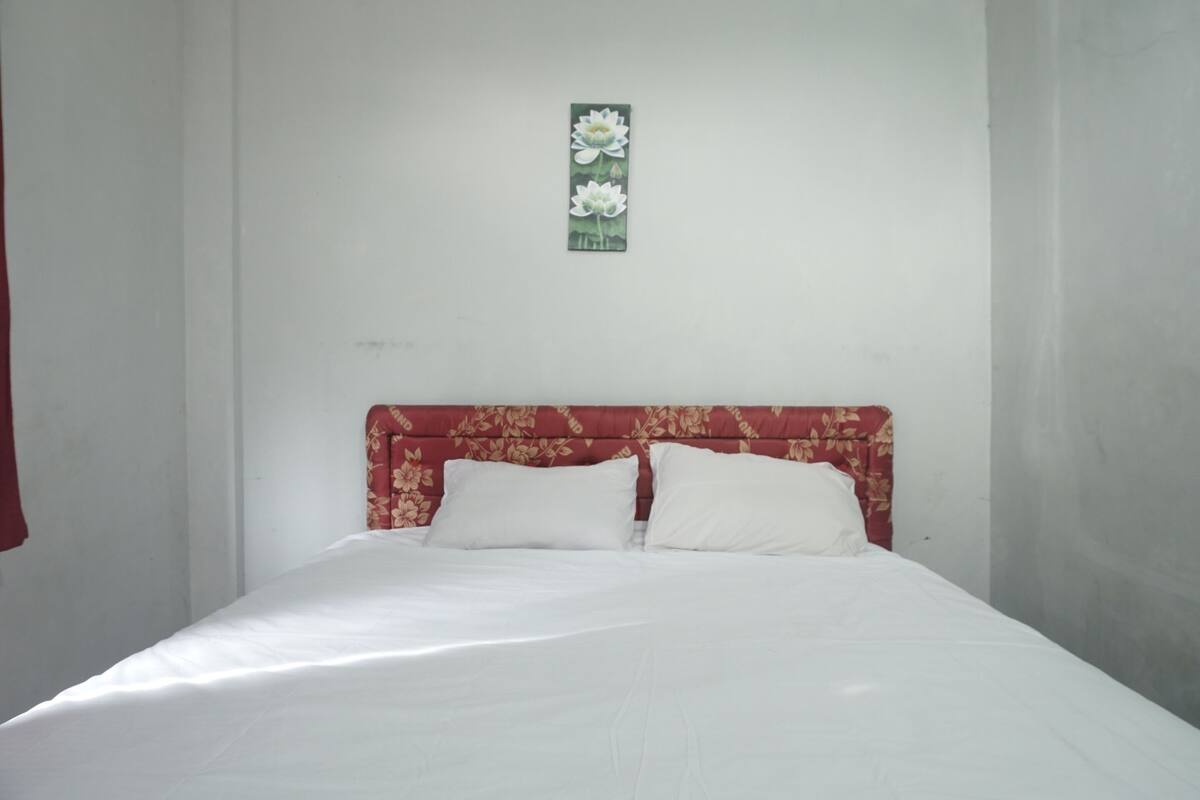 A bed with white bedding and a red floral headboard in a room with plain white walls.