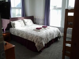 A hotel room with a large bed, a wooden nightstand, a desk, and a view of a body of water through the window.
