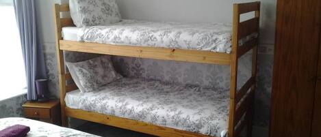 A bunk bed with floral bedding, a wooden wardrobe, and a small bedside table with a lamp.
