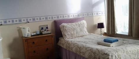 A bedroom with a bed, a nightstand, a dresser, a lamp, and a window with curtains.