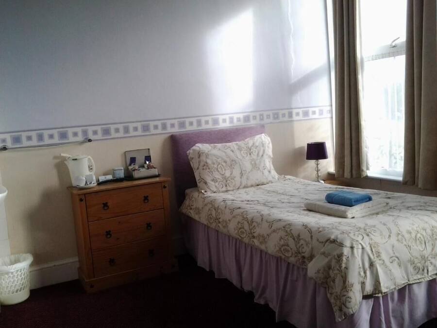A bedroom with a bed, a nightstand, a dresser, a lamp, and a window with curtains.