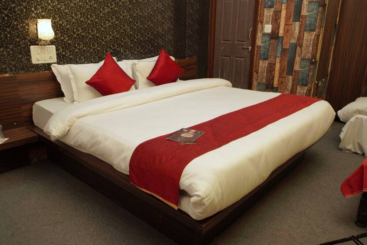 A neatly made bed with white linens and a red throw blanket, a wooden headboard, and a wall-mounted light fixture.