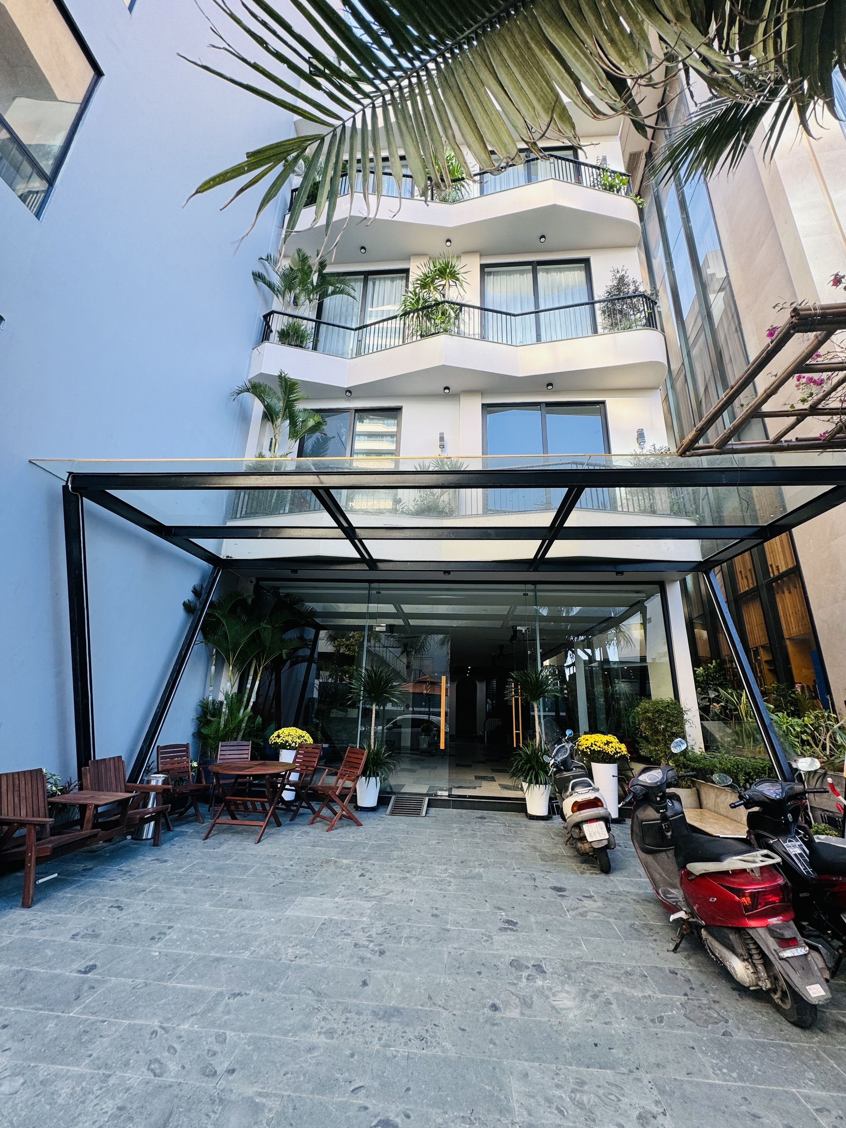 A modern building with a glass entrance, outdoor seating, and potted plants.