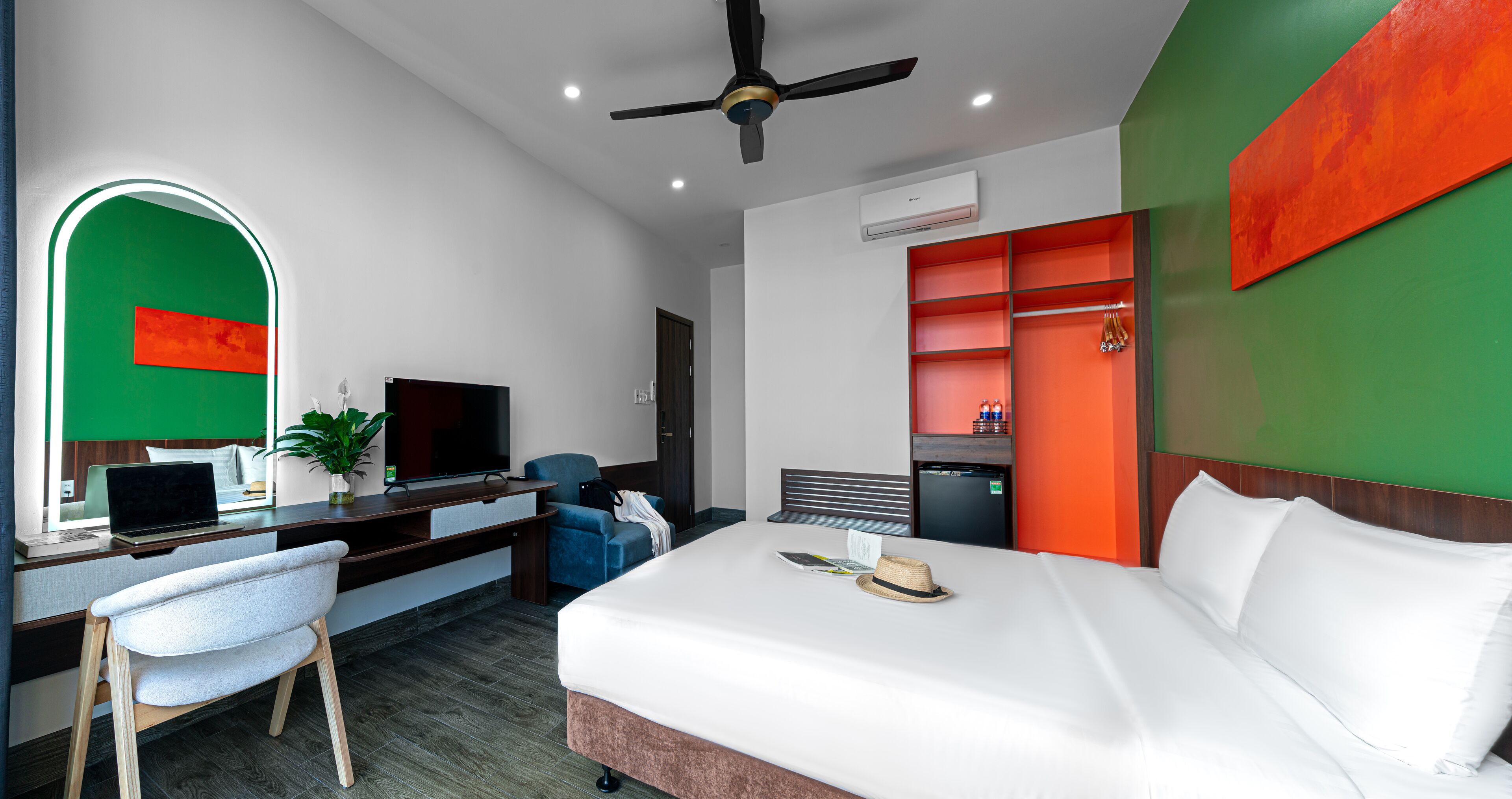 Una habitación de hotel moderna con cama, escritorio, silla, televisor y una pared de acento verde.