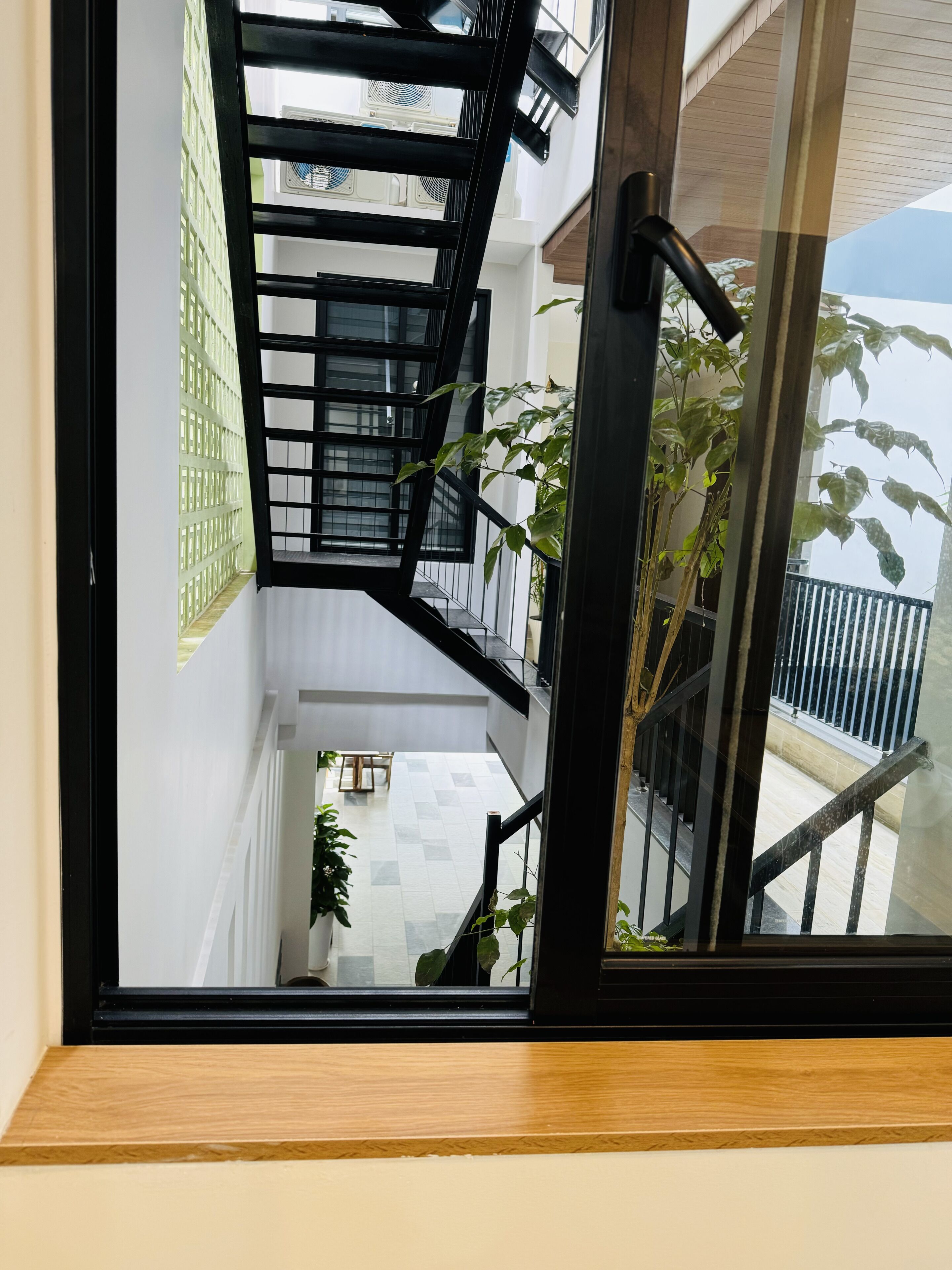 Una escalera moderna con barandales negros, paredes blancas y vistas al balcón exterior.