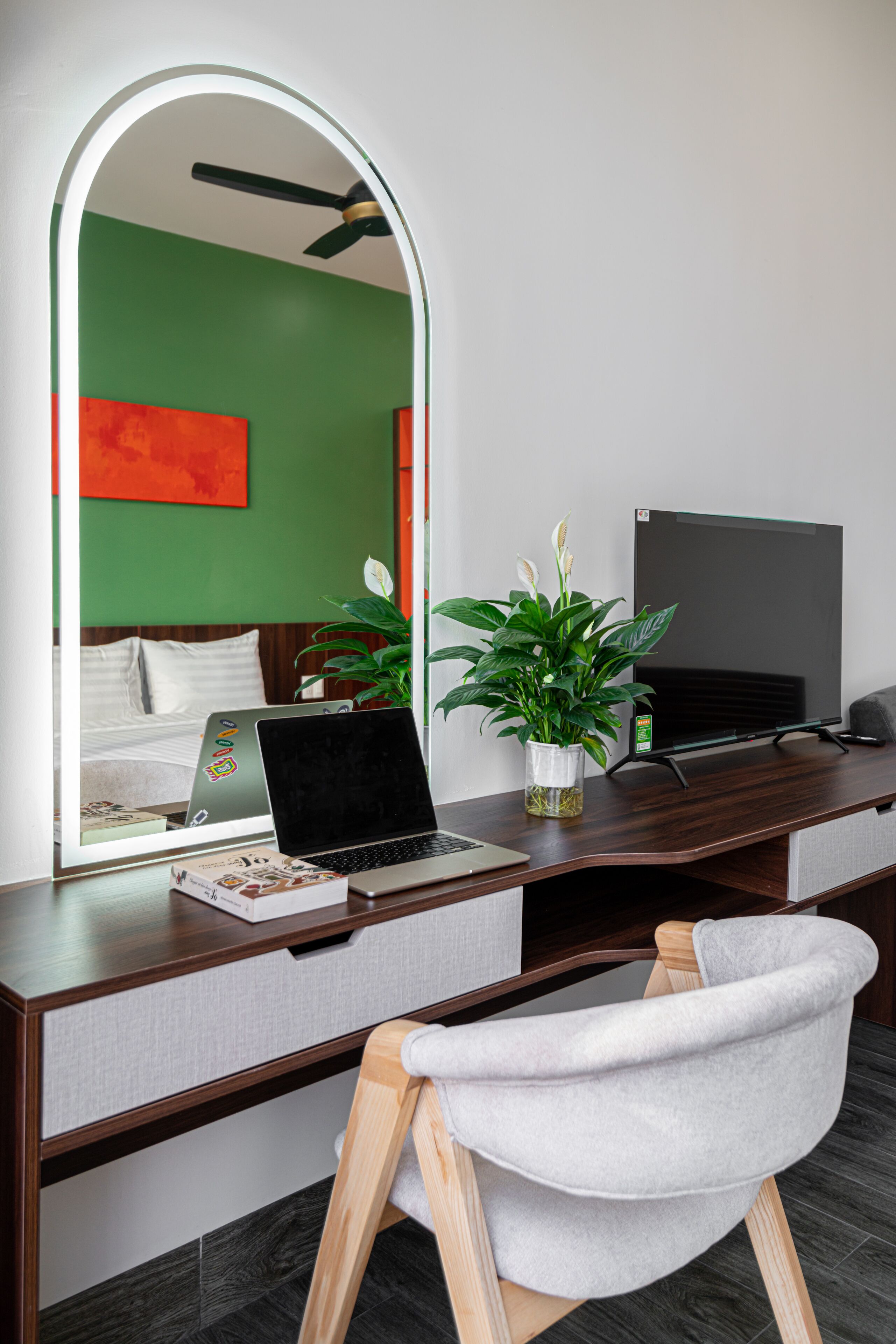 A modern hotel room with a desk, laptop, and a potted plant.