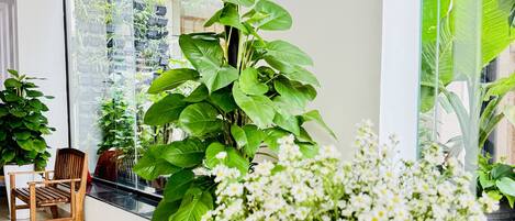 Un interior moderno con una mesa de madera, un jarrón blanco con flores y un ventanal con vistas a un jardín.