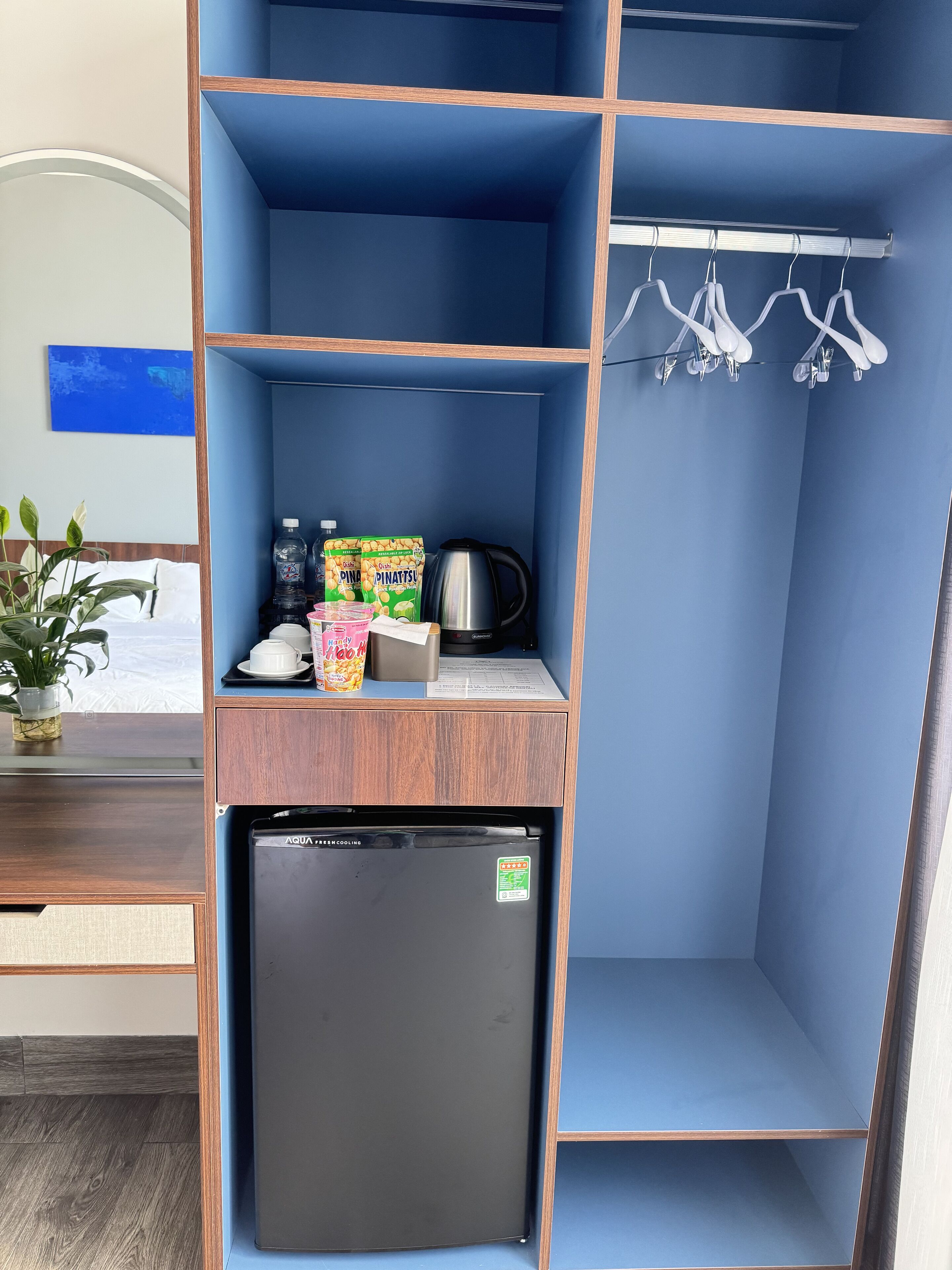 Une petite cuisine équipée d’un réfrigérateur noir, d’une machine à café, d’une bouilloire et de quelques produits alimentaires.