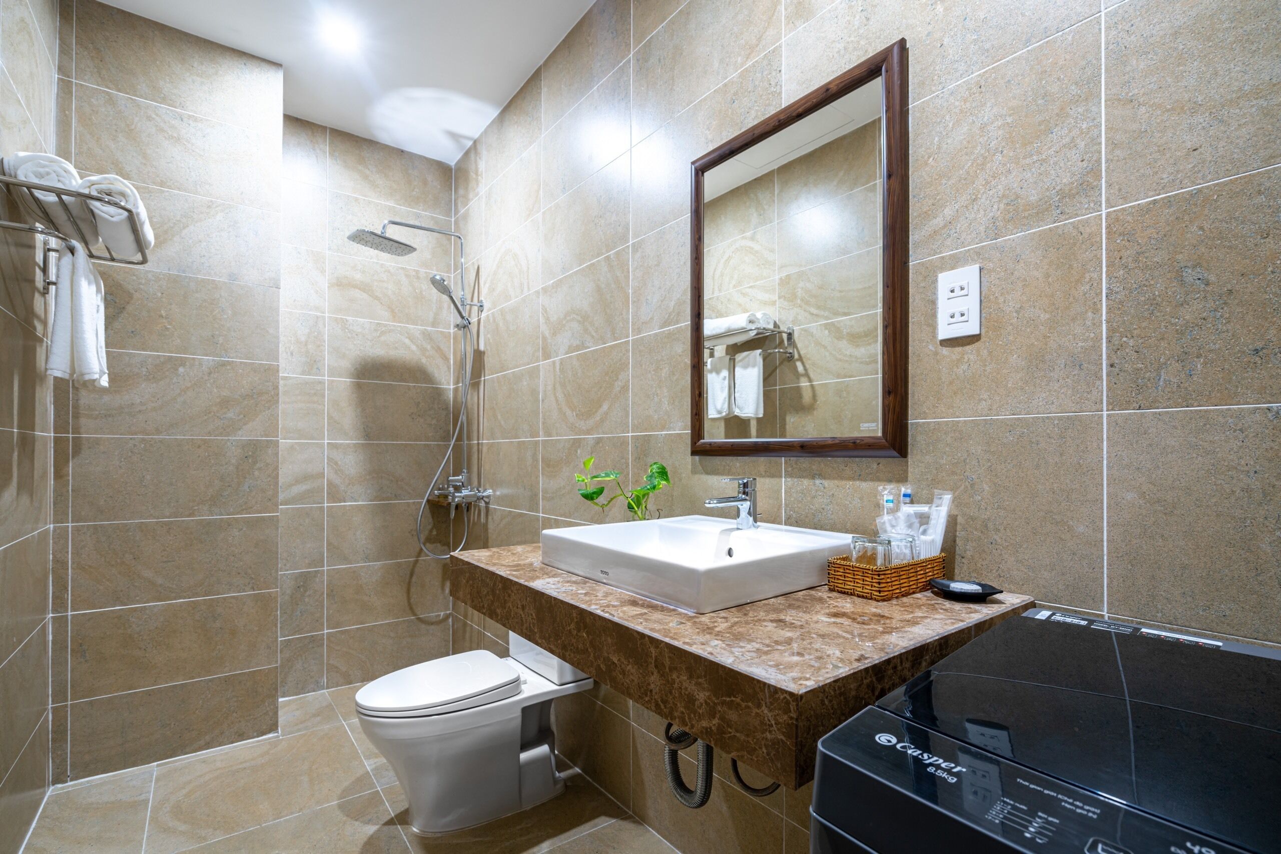 A modern bathroom with a white toilet, a sink with a marble countertop, a shower, and a large mirror.