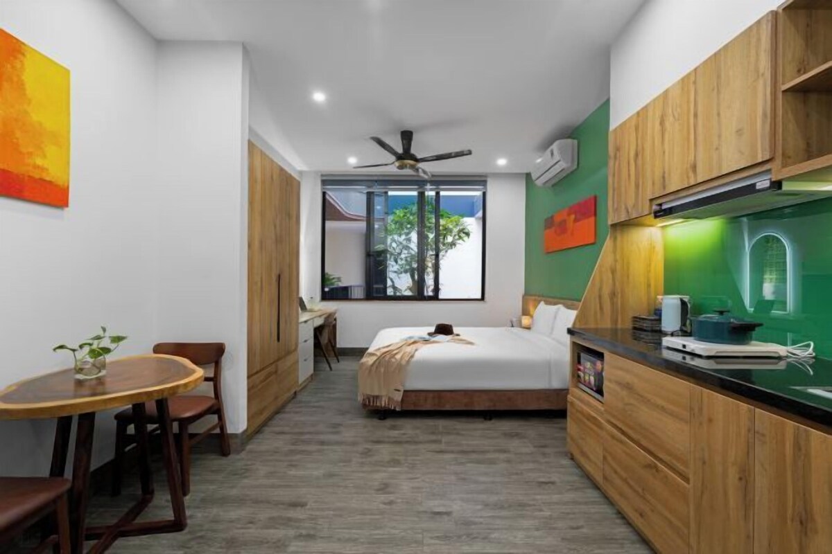 A compact hotel room with a bed, a small desk, a dining table, and a kitchenette.