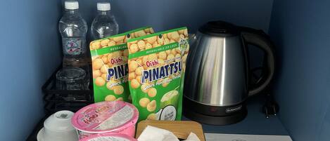 A kitchenette with a kettle, water bottles, snack packages, a coffee maker, and a menu.