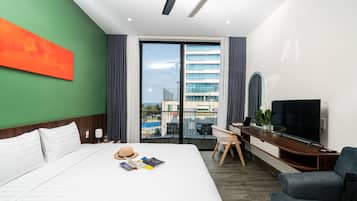 A hotel room with a bed, a desk, a TV, and a view of buildings and a pool.