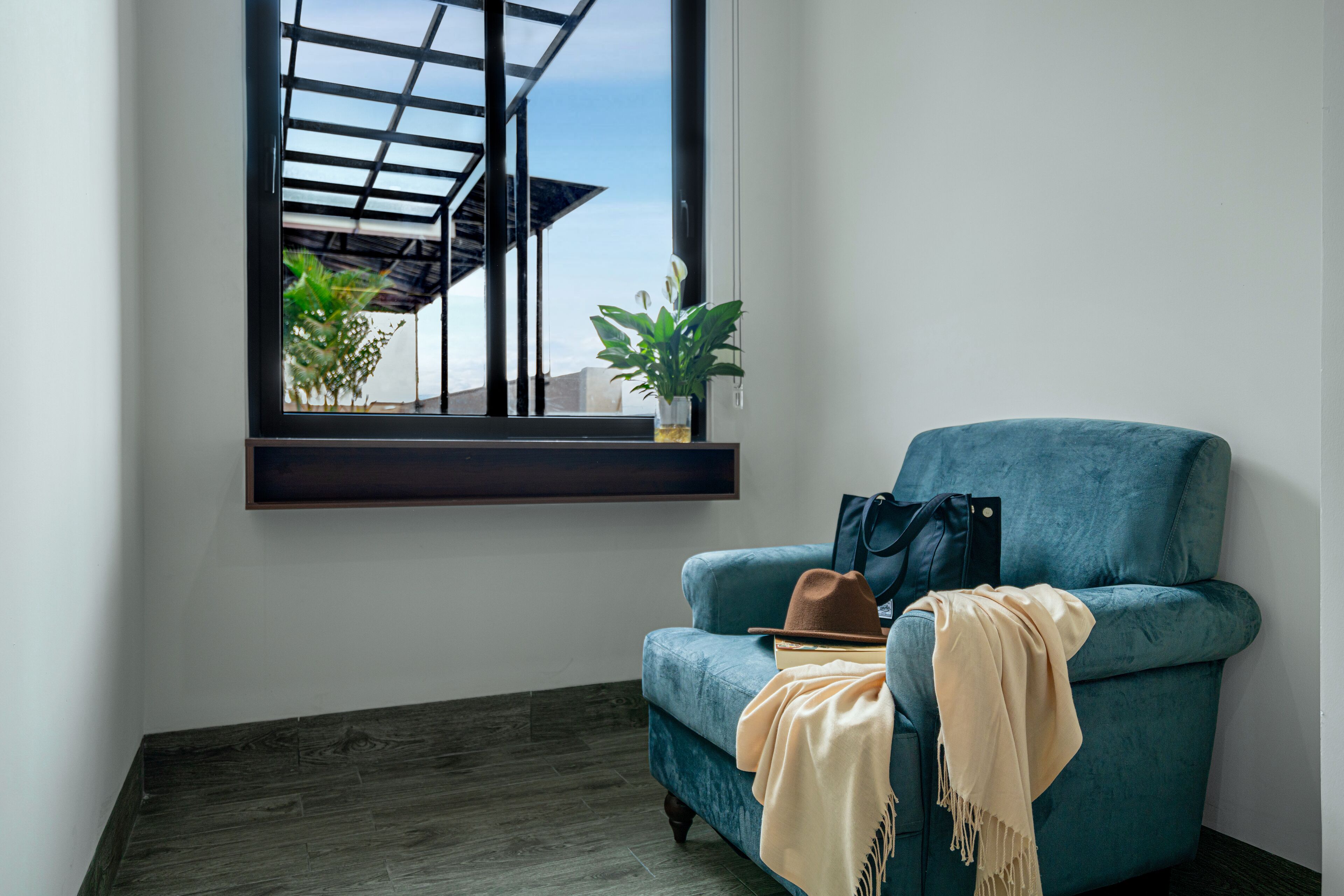 Ein Zimmer mit einem türkisblauen Sessel, einem Fenster mit Blick auf ein Gebäude und Pflanzen sowie einem Holzboden.