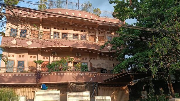 A multi-story building with balconies, a gated entrance, and parked trucks.