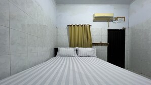 A small, narrow room with a bed, a curtain, an air conditioning unit, and a door.