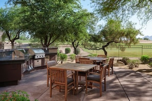 Un patio exterior con una parrilla, mesas y sillas de madera.