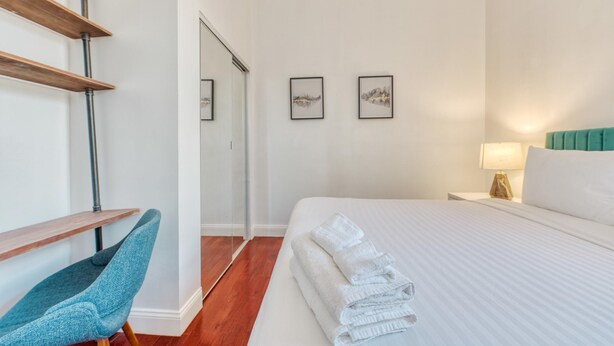 Habitación de hotel con una cama, una silla, un escritorio y dos cuadros en la pared.
