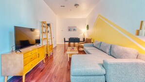 Una sala moderna con un sofá, televisión, mueble de madera y una escalera.