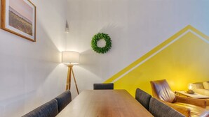 Un salón de conferencias con una mesa de madera, sillas grises, una lámpara de pie, una corona verde en la pared y una pared de acento amarilla.