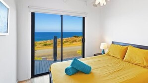 A bedroom with a bed, a nightstand, a lamp, and a view of the beach. - Ultimate Beachfront Retreat (Sunderland Bay)