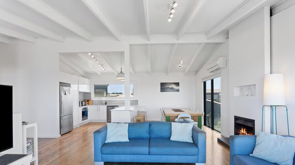 Een moderne woonkamer met een blauwe bank, een open haard en een keuken op de achtergrond.