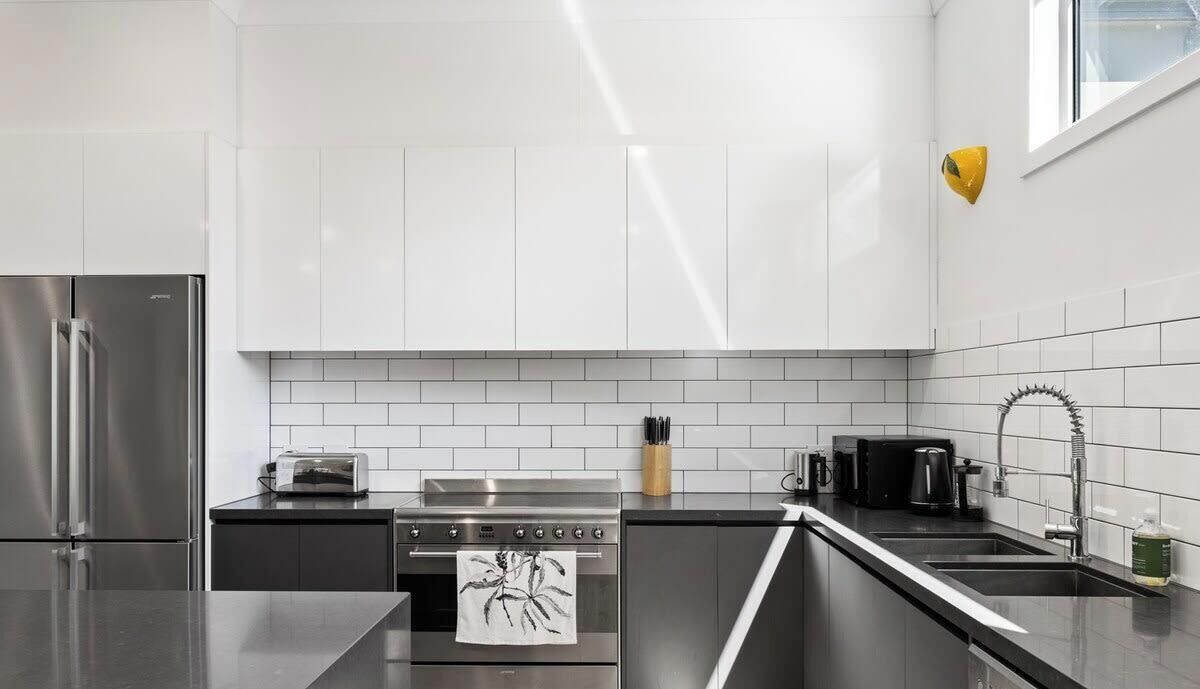 A modern kitchen with white cabinets, a stainless steel refrigerator, a stove, and a sink.