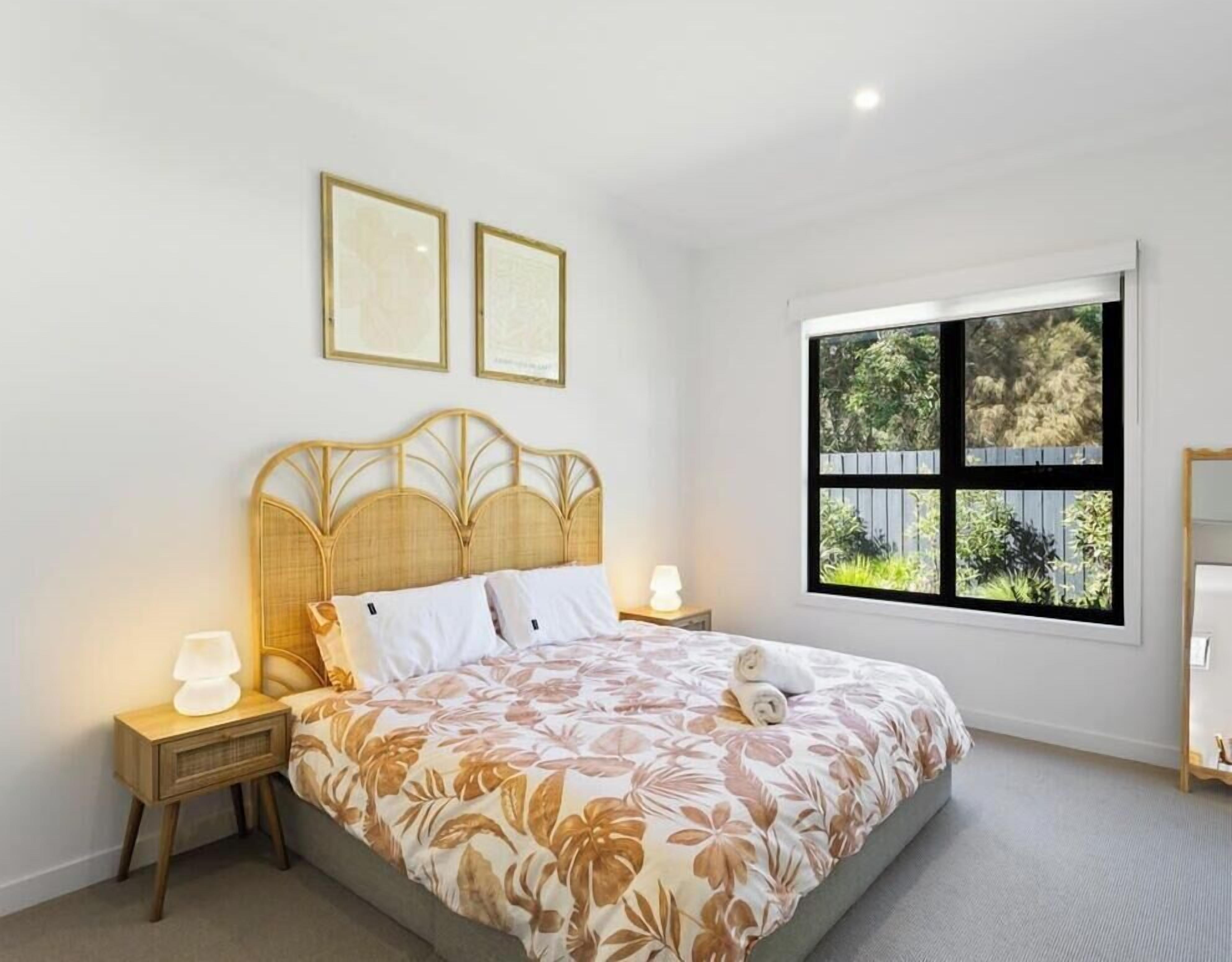 A bedroom with a bed, two bedside tables, a window with a view, and two framed pictures on the wall.