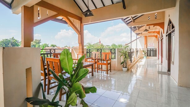 A covered outdoor area with tiled flooring, wooden chairs, and potted plants. - Hotel O Buduran Homestay Syariah (Sidoarjo)