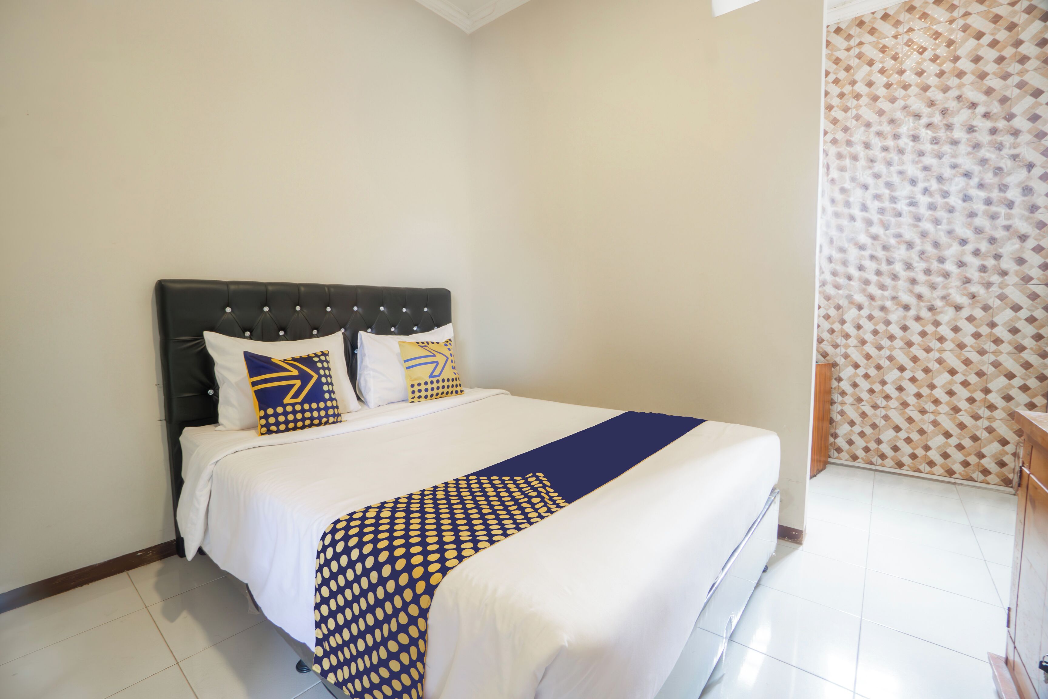 Un lit bien fait, recouvert d’une couvre-lit à motifs, avec une tête de lit noire en tissu et deux oreillers aux motifs géométriques.