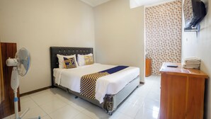 A hotel room with a bed, a bedside table with a remote control, a fan, and a wooden cabinet. - Hotel O Buduran Homestay Syariah (Sidoarjo)