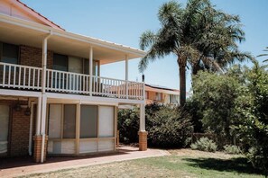 A two-story building with a balcony, brick walls, and a palm tree in the background.