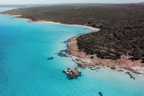 An aerial view of a coastal area with clear turquoise waters, a rocky shoreline, and dense forested hills. - Seascape - Where Coastal Fun and Adventure Meet (Eagle Bay)