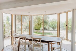 A sunlit room with a large window, a wooden table, and white chairs.