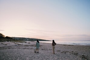 A beach with sand and water, a person walking, and another standing.