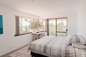 A bedroom with a bed, a desk, and large windows.