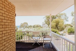 A covered outdoor area with a brick wall, a wooden deck, two white chairs, and a view of trees and a distant landscape. - Seascape - Where Coastal Fun and Adventure Meet (Eagle Bay)