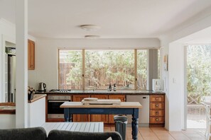 A kitchen with a large window, wooden cabinets, and a dining table. - Seascape—Coastal Adventure & Ocean Vistas (Eagle Bay)