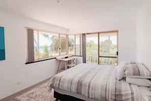 A bedroom with a bed, a desk, and large windows with a view. - Seascape - Where Coastal Fun and Adventure Meet (Eagle Bay)