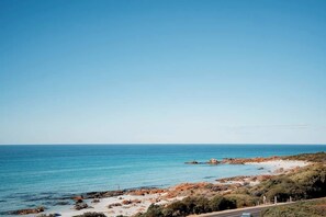 A coastal landscape with a clear sky, rocky beach, and a road leading to the sea. - Seascape - Where Coastal Fun and Adventure Meet (Eagle Bay)