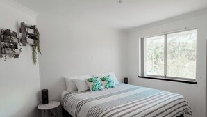 Een slaapkamer met een bed, een raam en een kleine tafel.