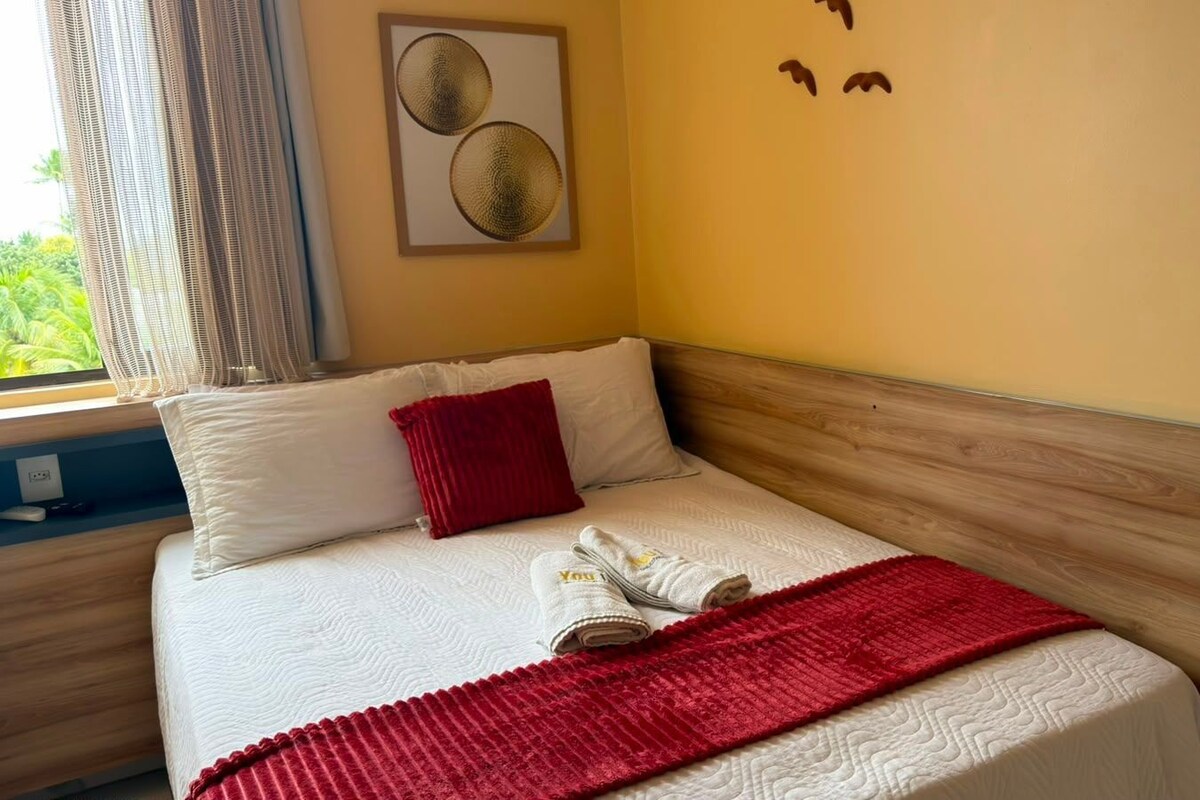 A hotel room with a bed, a red throw blanket, and a pair of towels.