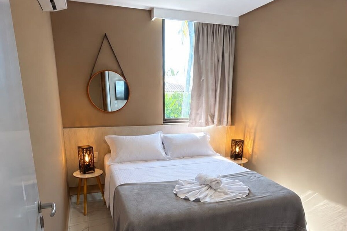 A hotel room with a bed, bedside lamps, a mirror, and a window with curtains.
